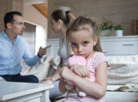 Little girl holding teddy bear while parents fight in background